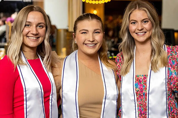 three women wearing Sigma Phi Alpha honor cords